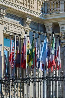 Facade of a historic building in Madrid with multiple international flags waving, representing diversity and global diplomacy. Ideal for politics and international relations themes. clipart