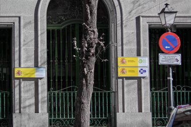 Madrid, Spain - January 19, 2025: Spain's Ministries of Inclusion, Health and Consumer Affairs on a building in Madrid. It features arched windows with green bars, a no-parking sign and vegetation. clipart