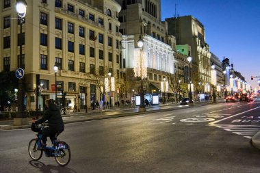 Madrid, İspanya - 24 Ocak 2025: Madrid, İspanya 'da Gran Via' nın gece manzarası, aydınlatılmış binalar ve ön planda bir bisikletçi. Kentsel, seyahat ve mimari temalar için