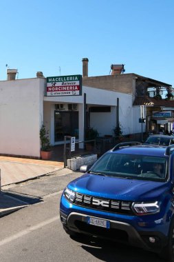 Civitavecchia, Italy - January 26, 2025: Italian butcher shop in Civitavecchia, with a sign with Macelleria Baiocco Norcineria and parked vehicles. A pedestrian stands near a black car clipart