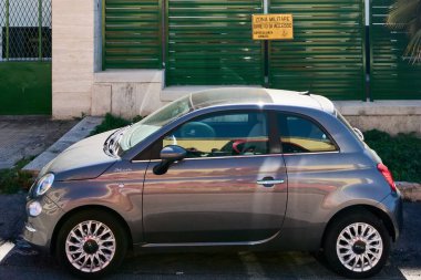 Civitavecchia, İtalya - 26 Ocak 2025: Yeşil çitin yanına park edilmiş küçük bir araba ve sarı askeri bölge işareti, sivil araç ile yasak bölge arasındaki zıtlığı vurguluyor.