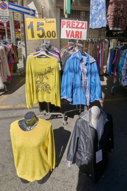 Civitavecchia, İtalya - 26 Ocak 2025: Açık hava pazarında renkli kıyafetlerin gösterimi. 15 avrodan başlayan fiyatları gösteren bir tabelayla askılara çeşitli elbiseler asılıyor ve düzenleniyor.