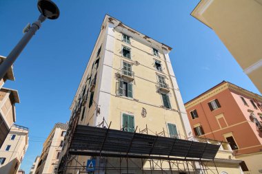 Yeşil panjurlu ve görünür giysili bir bina. İnşaat iskelesi binanın alt kısmını çevrelemiş..