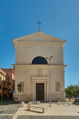 Civitavecchia, İtalya - 27 Ocak 2025: Civitavecchia, İtalya 'daki tarihi kilise. Sokak manzarası park halindeki arabaları ve açık mavi gökyüzünü içeriyor, İtalyan kültürünü gösteriyor.