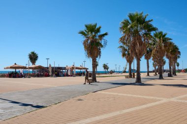 Civitavecchia, İtalya, 31 Ocak 2025: Palmiye ağaçları ve sahil kenarındaki kafelerle kaplı güneşli gezinti alanı. Ziyaretçiler okyanusa bakan geniş meydanda yürürler ve rahat bir sahil atmosferinin tadını çıkarırlar..