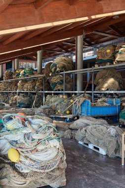 A portside fishing net repair area filled with commercial fishing gear. Shelves hold layers of nets, ropes, and floats, vital for the fishing trade. clipart