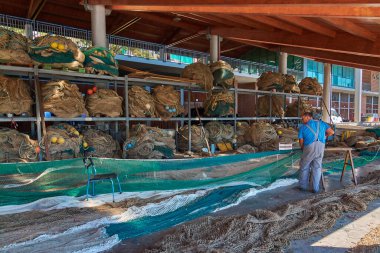 Civitavecchia, İtalya - 31 Ocak 2025: Bir balıkçı iyi organize edilmiş bir depoda balık ağlarını titizlikle onarıyor. Bu resim ağ bakımının ayrıntılı sürecini vurgular.