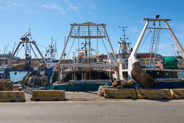 Civitavecchia rıhtımında balıkçı tekneleri, ağlar ve makaralar da dahil olmak üzere çeşitli balıkçılık malzemeleriyle donatılmış. Bu resim, balıkçılık operasyonlarının ayrıntılı ve organize kurulumunu betimler