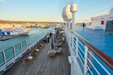 Civitavecchia, İtalya - 6 Şubat 2025: Ahşap döşemeli ve oturma alanlı bir yolcu gemisinin alt güvertesinde dinlenen yolcular, liman kenti Civitavecchia 'nın huzurlu manzarasının keyfini çıkarıyorlar.