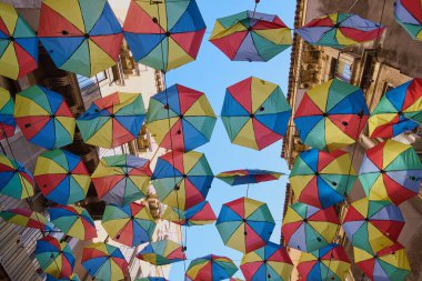 Göz kamaştırıcı renkli şemsiyeler güneşli bir gökyüzünün altında asılı duruyor ve şehir manzarasına neşe katıyor. Kavram: Gökyüzü dekorasyonu