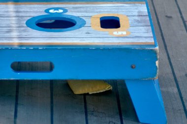 Close-up of beanbag lying on wooden surface beneath a colorful cornhole game, perfect for sunny outdoor leisure settings. clipart