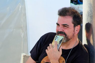 Sarı yıpranmış bir çanta ve çiziklerle cep telefonu tutan sıradan bir adam, kordona gözlük takıyor ve dışarıda siyah bir gömlek giyiyor..