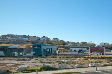 Girit. Yunanistan - 27 Mart 2025: Yunanistan 'ın Girit kentinde şehir binaları ve açık gökyüzüyle çevrili açık bir alana parketmiş çeşitli renklerde otobüsler bulunan bir otobüs parkı.