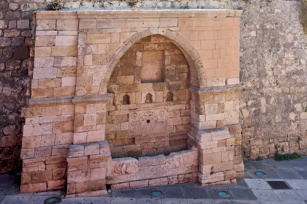 Girit, Yunanistan - 7 Nisan 2025: Osmanlı çeşmesi Jenitsar Aga, asfalt bir alanla çevrili zarif kabartmalar ve geometrik tasarımlar sergiliyor. Heraklion 'daki kültürel mirası yansıtan tarihi bir mücevher.