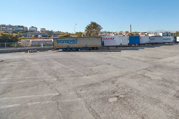 Girit, Yunanistan - 7 Nisan 2025: Çitler ve ağaçlarla çevrili kamyonet park alanı, Girit 'te geniş alan ve kentsel yakınlığa sahip lojistik araçların planlarını vurguluyor.