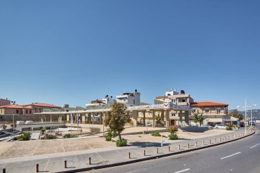 Girit. Yunanistan - 11 Nisan 2025: Açık mavi gökyüzünün altındaki sakin bir Yunan köyünde resmi afişleri ve geleneksel mimarisi bulunan modern kıyı belediye binası