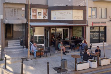Girit. Yunanistan - 11 Nisan 2025: Müşterilerin rahat bir atmosferde içki içtiği açık hava koltuklu büyüleyici bir kafe. Yunanca işaret ve kentsel unsurlar otantik yerel deneyimi artırıyor.
