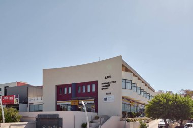 Girit. Yunanistan - 23 Nisan 2025: Çağdaş adli tıp araştırma tesisi güneşli bir sokakta, ağaçlar ve kentsel bir ortamda ticari tesislerle çevrili resmi tabelalı.
