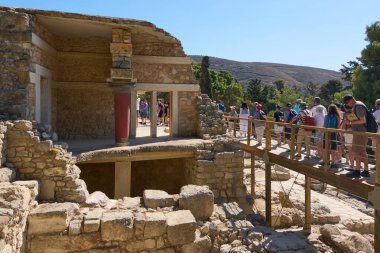 Girit. Yunanistan - 26 Nisan 2025: Knossos Sarayı 'nın tarihi bölgesinde, antik Minos kalıntıları, ikonik sütunlar ve mavi gökyüzü ile çevrili ahşap bir köprüde yürüyen turistler.