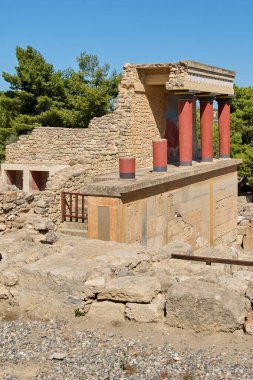 Knossos Sarayı 'nın tarihi mekanında Girit' teki Minos mimarisinin sanatsal mirası ve kültürel önemini vurgulayan antik kalıntılar arasında duran canlı kırmızı ve siyah sütunlar yer alıyor..