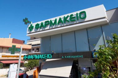 Girit. Yunanistan - 05 Mayıs 2025: Yunanistan 'da bir eczane büyük yeşil bir haç ve eczane vitrininde Yunan harfleri sergiliyor ve ilave diş sağlığı kliniği tabelasıyla birlikte tıbbi malzeme ve reçetelerin yerini açıkça belirtiyor..