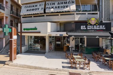 Girit. Yunanistan - 05 Mayıs 2025: Tıbbi yardım sunan bir eczane ve işaretlenmiş taco ve kokteylleri olan bir restoran gösteren bir şehir manzarası. Şehir merkezi sembolik etkinliklerle zenginleşti..
