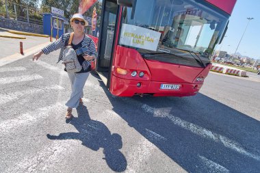 Girit. Yunanistan - Mayıs 05, 2025: Meşgul bir otobüs durağında kırmızı Heraklion Hattı 'ndan çıkan bir yolcu. Beyaz zemin işaretleri ve istasyon işaretleri kentsel ulaşım ayarlarını vurguluyor.