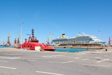 Girit. Yunanistan - 05 Mayıs 2025: Costa Fortuna yolcu gemisinin yer aldığı bir deniz sahnesi, kırmızı bir römorkör ve kargo operasyonları için kullanılan yüksek vinçler. Açık hava, eğlence ve endüstri arasındaki zıtlığı artırır..