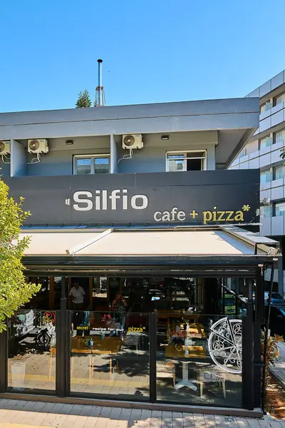 Girit. Yunanistan - 05 Mayıs 2025: Görüntü, Silfio Cafe ve Pizza 'nın dış cephesi, parlak gri bir cephe, büyük pencereler ve pizzasının gizli bir tarifini ön plana çıkaran markalar sergiliyor.