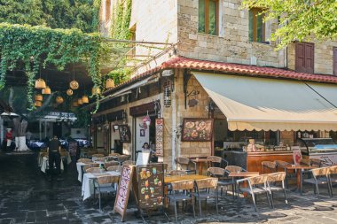 Rhodes. Yunanistan 24 Mayıs 2025: Boş masaları ve sandalyeleri olan, büyüleyici doğal elementler ve hafif aydınlatmalarla süslenmiş, sakin bir yaz akşamı atmosferi yaratan bir restoranda fresk al fresk yemek.