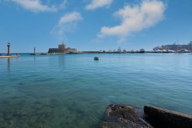 Rodas.Yunanistan - Haziran 04, 2025: Saint Nicholas Kalesi, deniz feneri, botlar ve parlak mavi gökyüzü altındaki yolcu gemisiyle Mandraki Limanı 'nın geniş manzarası