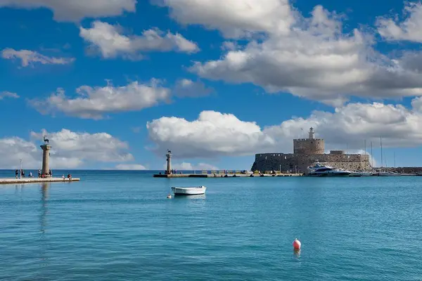 Rodas.Yunanistan - Haziran 04, 2025: Mandraki Limanı 'nın nefes kesici manzarası, tarihi Aziz Nicholas Kalesi, deniz fenerleri ve dinamik bulutlu gökyüzü altında çeşitli tekneler sergileniyor..