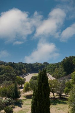 Yunanistan 'ın Rodos kentindeki antik stadyumun panoramik manzarası, bulutlu mavi gökyüzü altında duruş ve yemyeşil, miras için ideal..