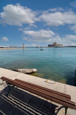 Mandraki Limanı 'nın rahatlatıcı manzarası, tarihi Aziz Nicholas Kalesi ve bulutlu gökyüzünün altındaki sakin sular..