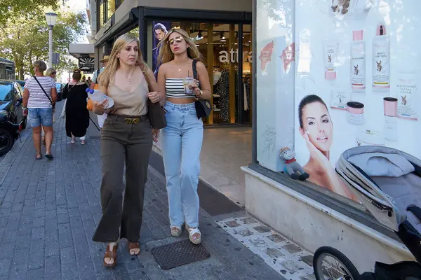 Rodas.Yunanistan - Haziran 04, 2025: Rodos 'ta bir alışveriş caddesinde günlük hayatı tasvir eden dükkanlar ve yayalarla yürüyen iki kadın.