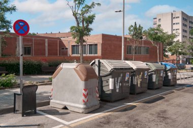 Viladecans.Barcelona - 29 Haziran 2025: Park levhası olmayan bir caddenin yanında büyük bir sıra geri dönüşüm kutusu, kentsel atık yönetimi ve çevre sorumluluğunu simgeliyor.