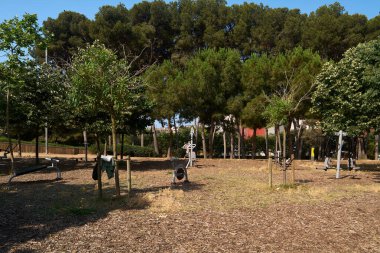 Viladecans.Barcelona - 2 Temmuz 2025: Güneşli bir parkta çeşitli açık hava egzersiz makineleri, kamu sağlığı ve sağlığı için ücretsiz fitness seçenekleri sunuyor