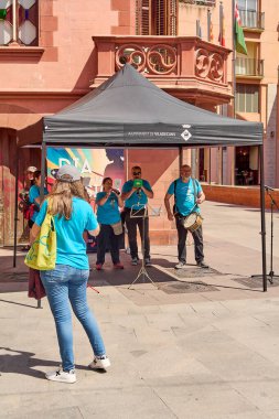 Viladecanlar. Barselona - 25 Temmuz 2025: Parlak mavi gömlekli ve arka planda tarihi bir bina cephesi bulunan bir yaz sokak konserinin şenlikli atmosferini yakalamak.