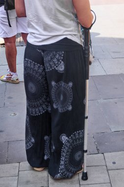 Güneşteki şehir kaldırımlarında hareketlilik yardımı kullanan yalnız bir kadın. Kentsel ortamlarda sağlık, destek ve zarafet için ideal.