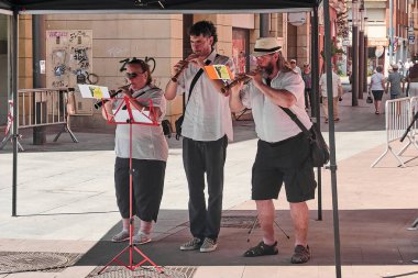 Viladecanlar. Barcelona - 25 Temmuz 2025: Güneşli bir günde, Viladecan caddesinde rüzgâr enstrümanları çalan üç müzisyen, açık havada canlı bir performans yakaladılar.