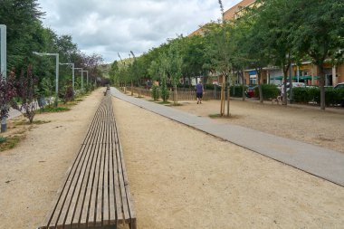 Viladecans.Barcelona - 28 Temmuz 2025: Halka açık bir park yürüyüş yolunun perspektif görünümü, kentsel çevrede tefekkür ve rahatlamaya yol açıyor.