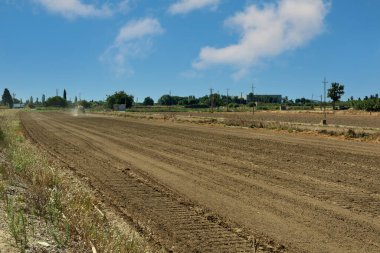 Bir traktör, bir yaz günü ekili geniş bir tarlada toprağı sürerek toprağın çalışmasını ve hazırlanmasını gösterir..