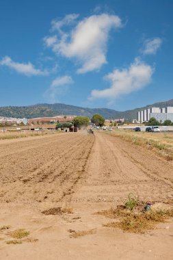 Viladecanlar. Barselona - 14 Ağustos 2025: Yerleşim alanı ve dağlara bakan çorak bir tarlanın perspektifi, doğa ve kentleşme arasındaki bağlantıyı gösteriyor.