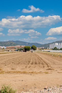 Viladecanlar. Barselona - 14 Ağustos 2025: Yerleşim alanı ve dağlara bakan çorak bir tarlanın perspektifi, doğa ve kentleşme arasındaki bağlantıyı gösteriyor.