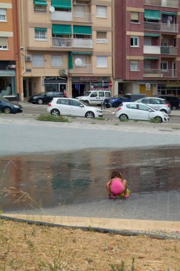 Viladecanlar. Barcelona - 2 Eylül 2025: Pembe takım elbiseli küçük bir kız halka açık bir çeşmede çömelmiş, kaygısız çocukluğu ve yaz tatilini kapsayan bir resim.