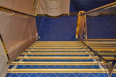 Yüksek açılı merdiven manzarası var. Halı, mavi ve altın tonlarda lüks bir geometrik desen içeriyor..