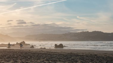 Meron sahilinde gün batımında San Vicente de la Barquera, Cantabria 'da iki sörfçü. İspanya.