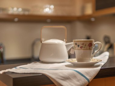 CUP OF TEA AND WHITE TEAPOT IN WARM KITCHEN. HOMELIKE. RELAXING MOMENT. SELECTIVE FOCUS.