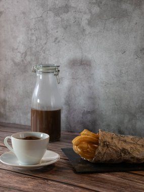 Tahta ve ahşap masa üzerinde churros ile bir fincan sıcak çikolatanın dikey fotoğrafı.