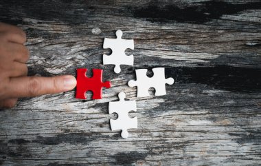 Kadınların elinde yapboz parçaları var. Tahta arka planda yapboz parçasının beyaz detayları. Bir iş ekibi olarak birlikte çalışma kavramı. Olaya dahil olma fikri, başarı için çalışmak..